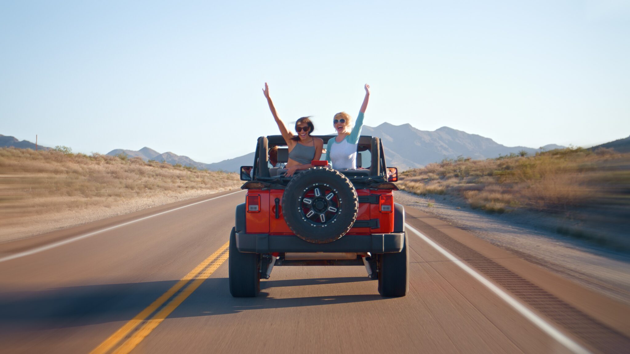 GettyImages-2188376661 Two people riding in the back of a red jeep