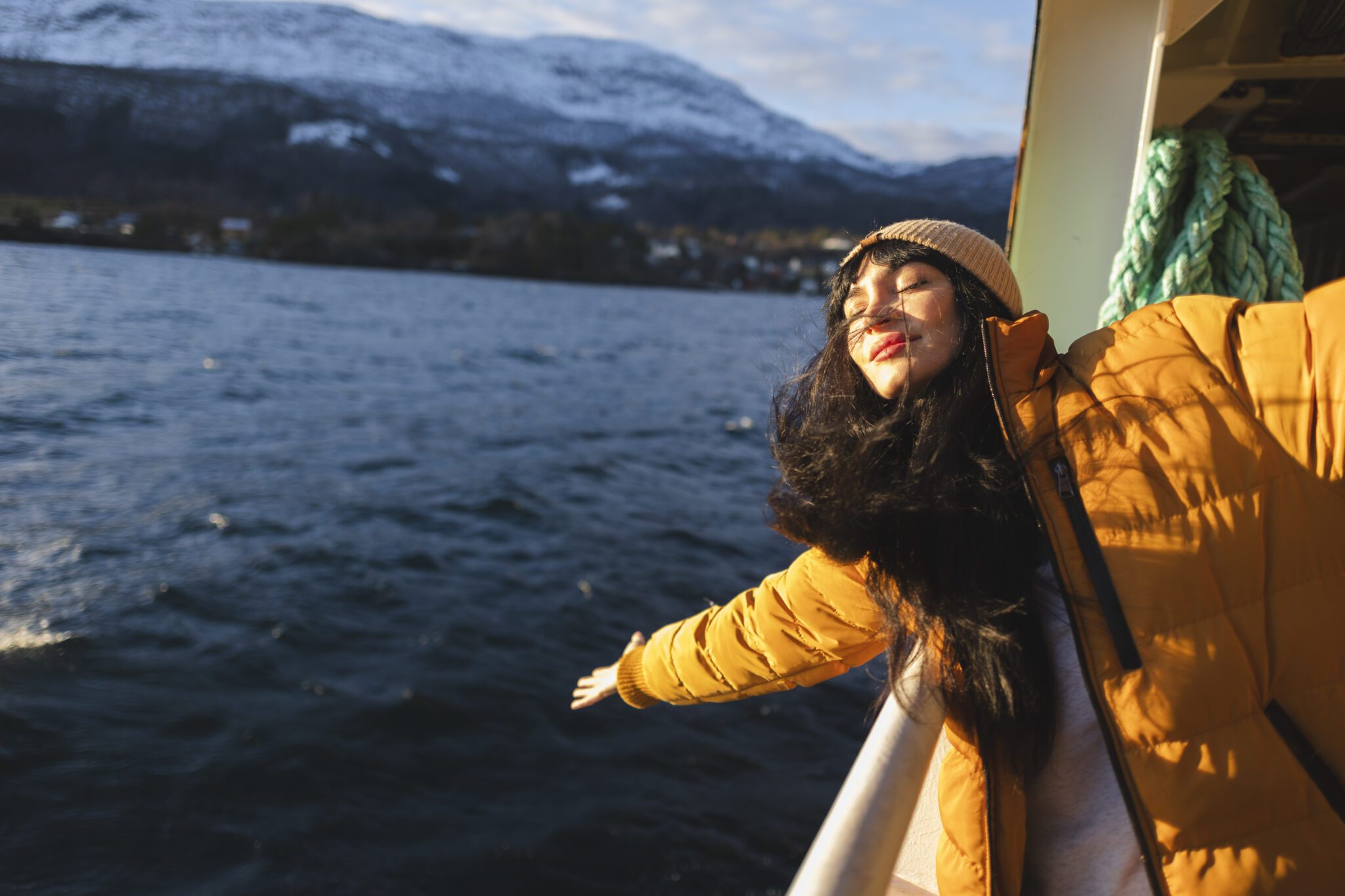 Cruise vacation travel woman enjoying freedom with open arms. A woman in yellow jacket on boat near body of water.