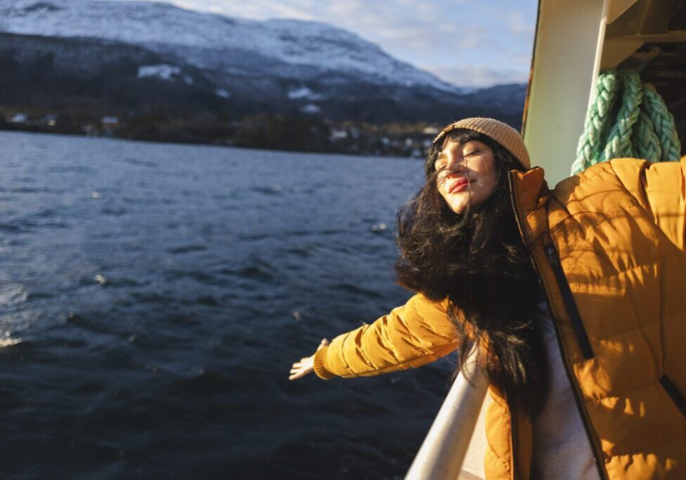 A woman in yellow jacket on boat near body of water.